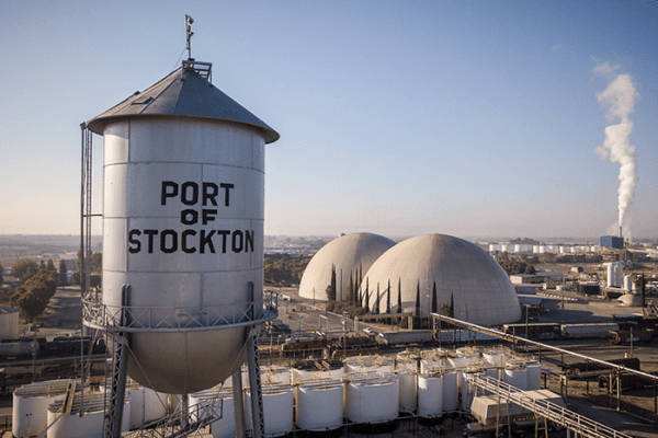 Image of water tower labeled "Port of Stockton", industrial facilities, and plume from a smokestack in the distance